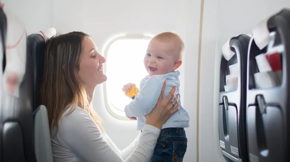 En skrattande bebis på ett flygplan. När man flyger med spädbarn är det bra att tajma när de sover och mata dem vid start och landning för att tryckutjämna öronen.